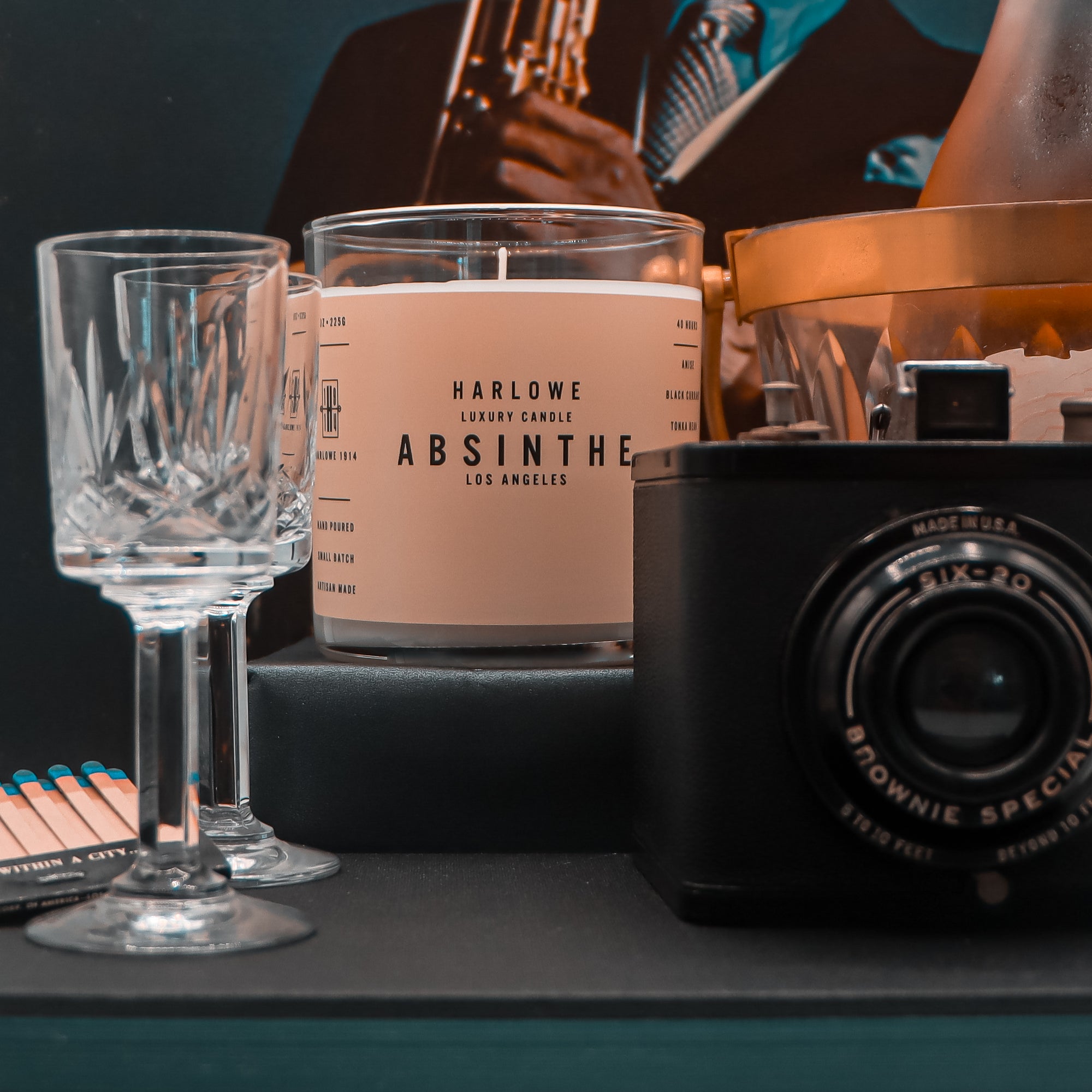 Harlowe Absinthe candle with a glass and camera on a dark surface