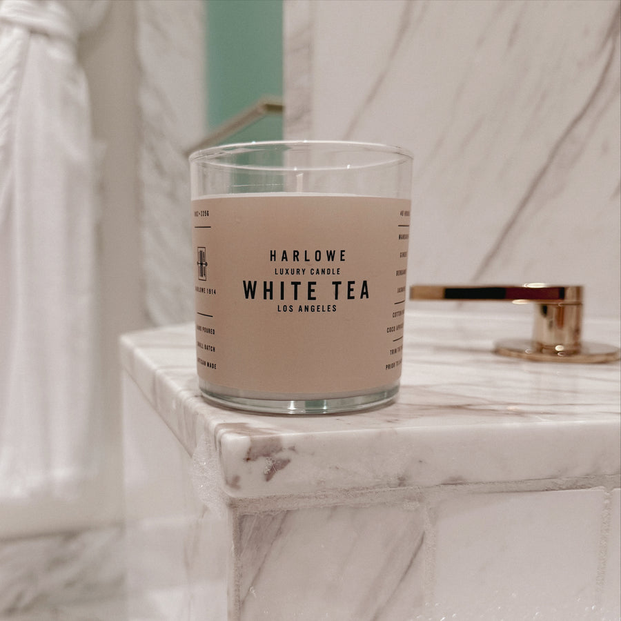 Harlowe White Tea candle on a marble surface next to bath tub